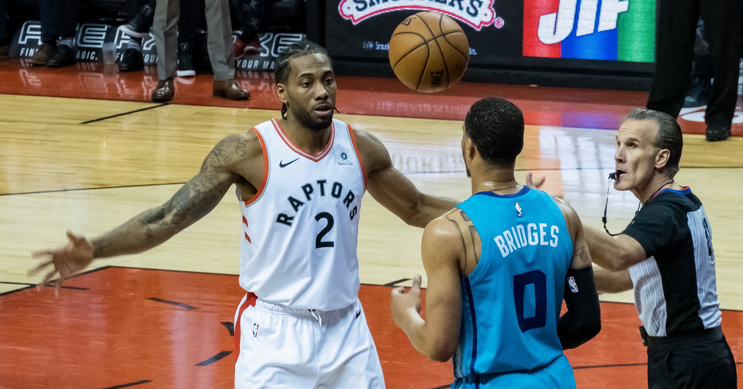 Kawhi Leonard and Miles Bridges face each other while both look at a basketball in the air above their heads, while a referee looks on. (📸 Chensiyuan via Wikimedia Commons under CC BY-SA 4.0.)